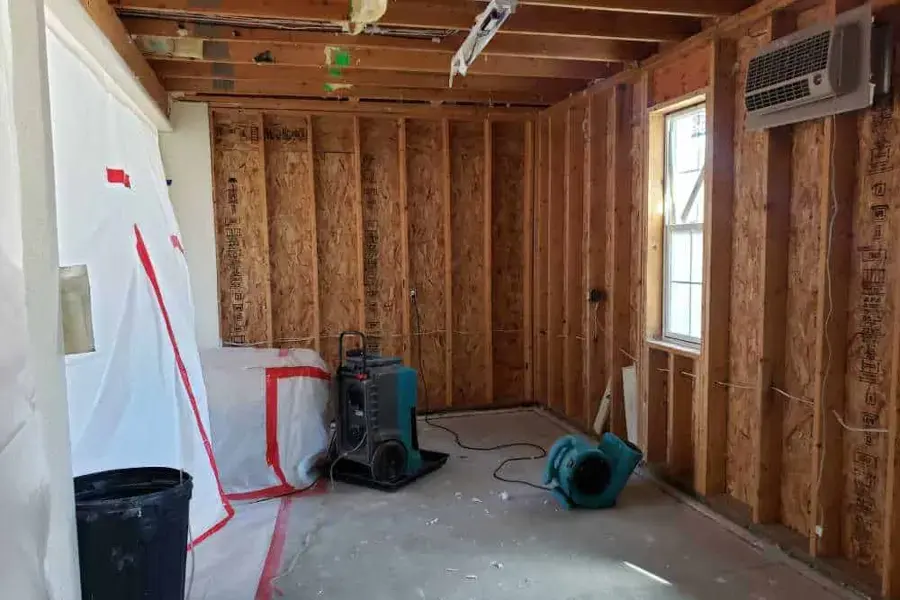 Opened wall framing with containment plastic, a dehumidifier and an air mover drying a room in a Lilburn home