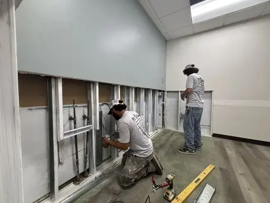 Two technicians opening a lower wall to reach supply pipes after a freeze